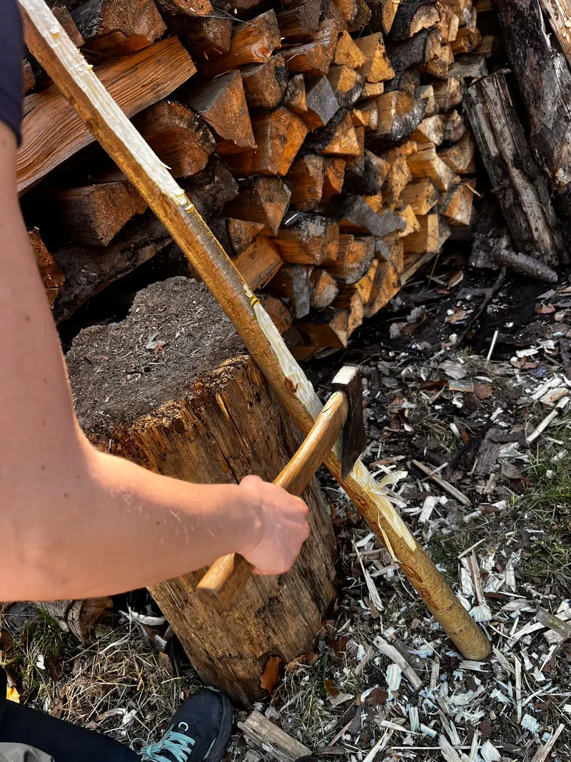 Ein Bogenrohling wird mit dem Beil auf dem Hackklotz bearbeitet