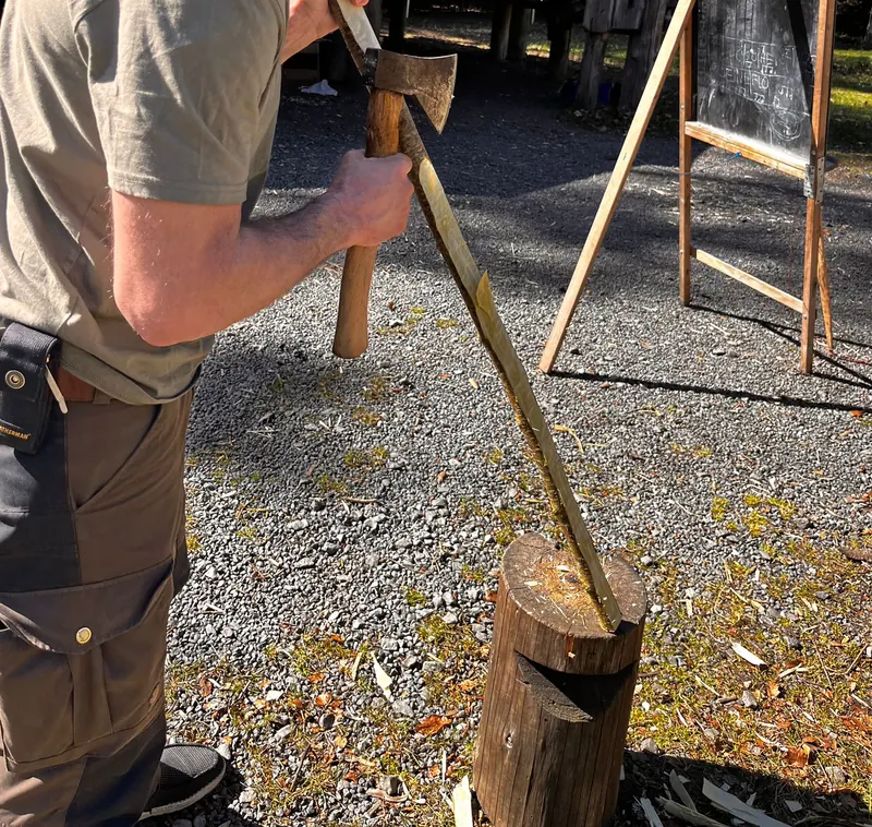 Mit dem Beil wird ein Holzstab auf dem Hackklotz gespalten